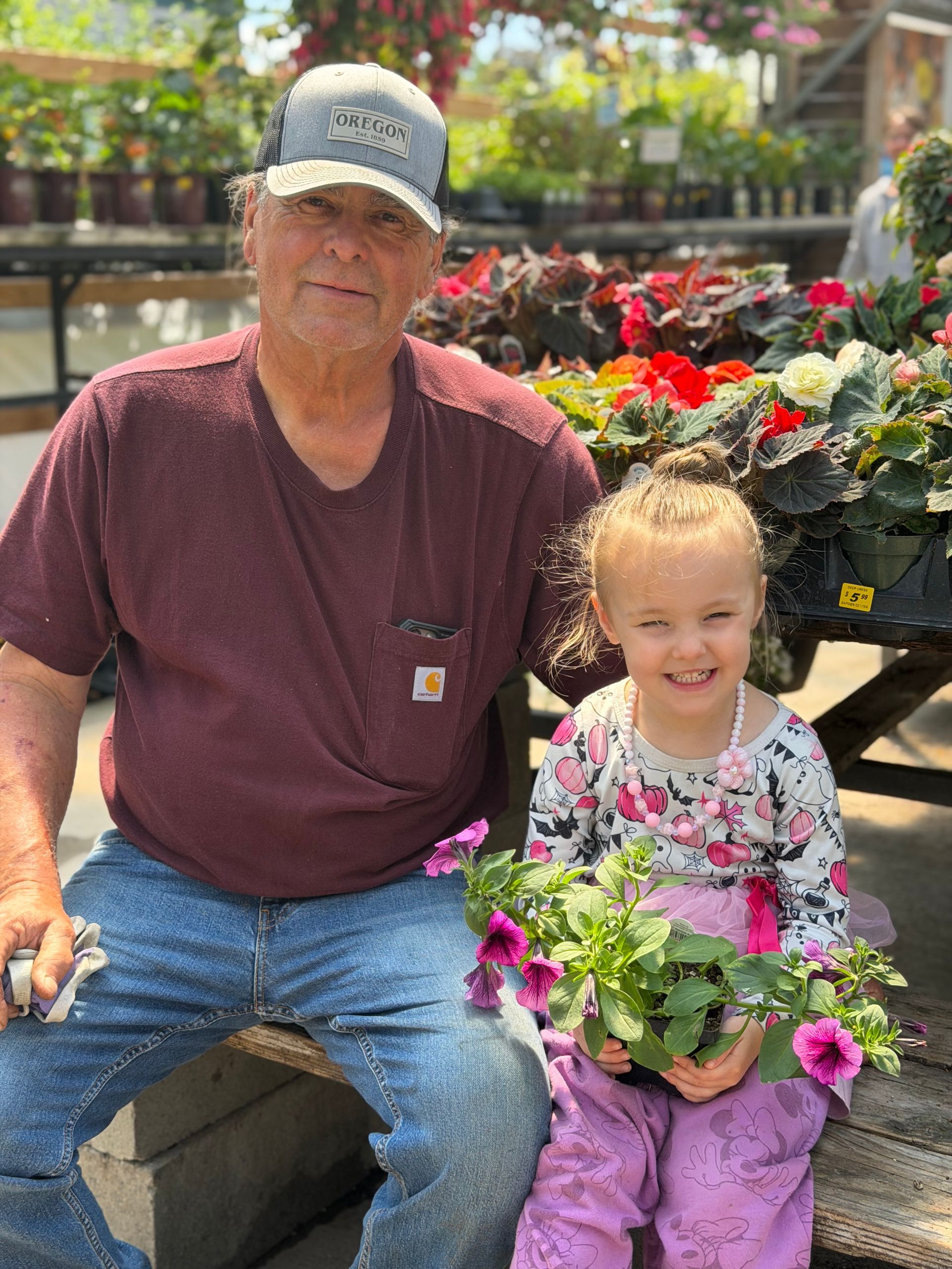 Man and child sitting beside colorful flowers outdoors, both smiling.