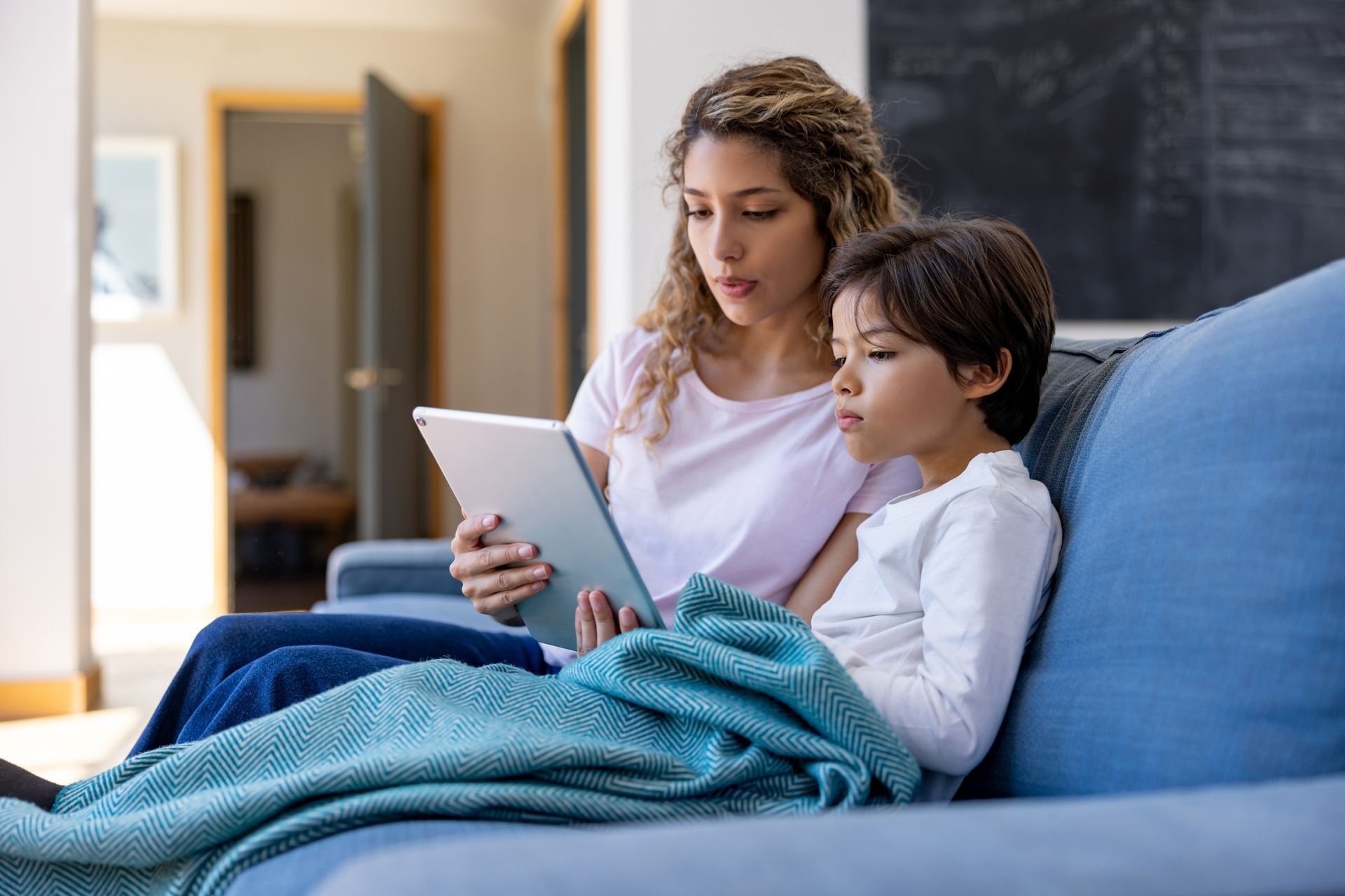 A woman and a child are sitting on a couch looking at a tablet.