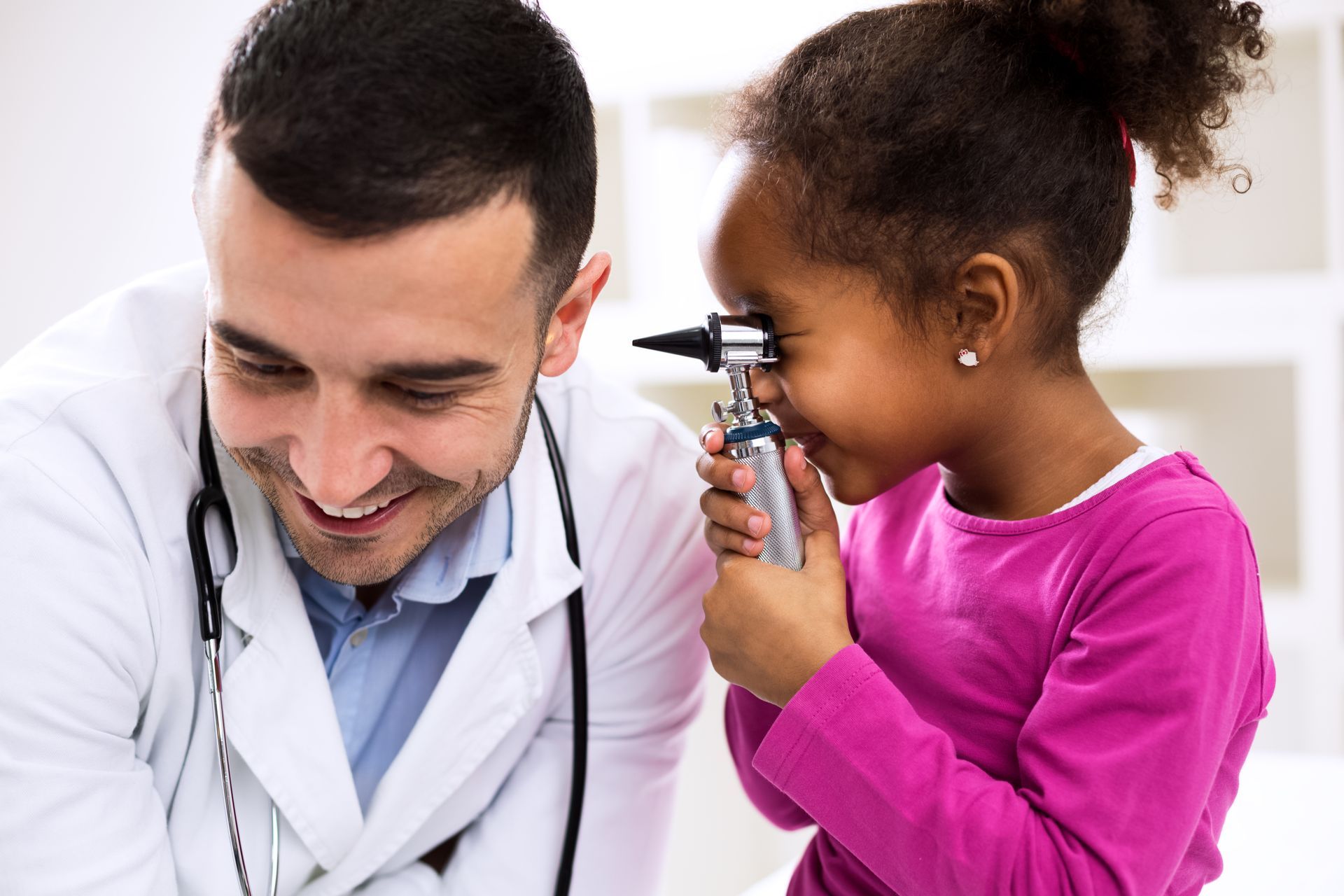 A woman is holding a baby while a doctor examines it with a stethoscope.