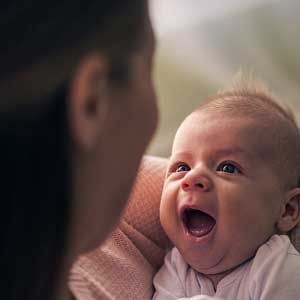 A woman is holding a baby in her arms and the baby is smiling.