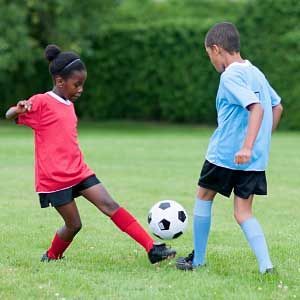A boy and a girl are playing soccer on a field.