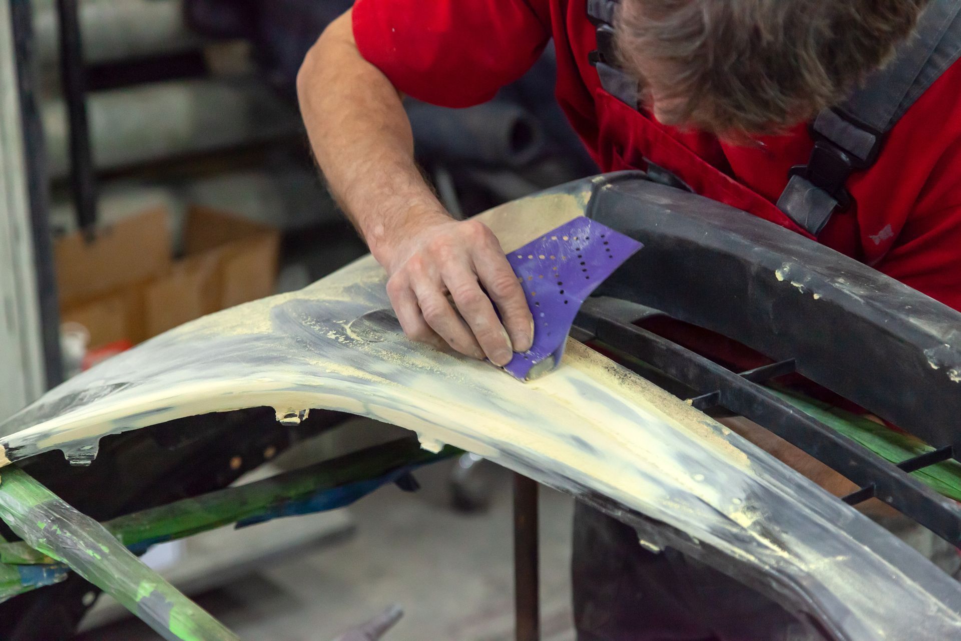 Person sanding a car body panel with a purple sanding block in a workshop