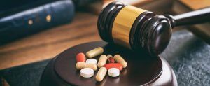 A wooden gavel rests on a sound block topped with an assortment of various prescription pills on a dark, leather surface.