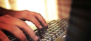 Close-up of hands typing on a laptop keyboard in a softly lit, warm environment.