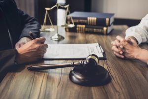 A legal consultation with a gavel, law books, and scales of justice on a desk between two people.