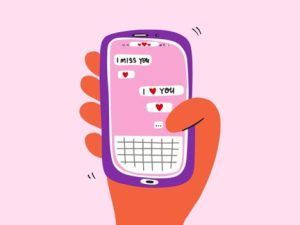 A hand holds a purple smartphone showing a pink screen with chat bubbles that say 