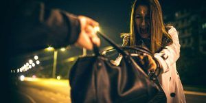 A person in a dark setting struggles to hold onto their black handbag as someone pulls it away.