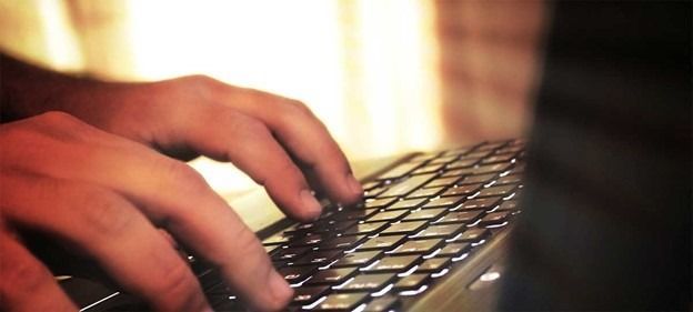 Hands typing on a backlit laptop keyboard in a dimly lit room.