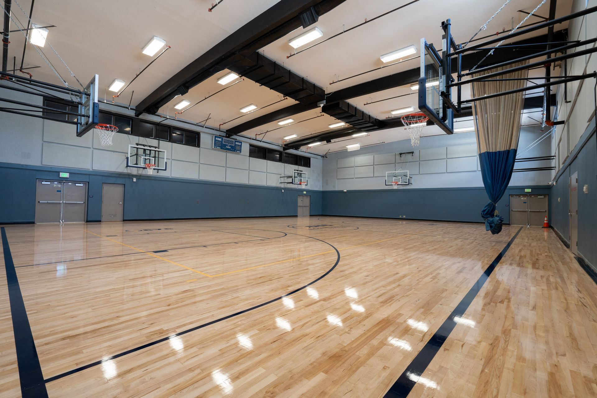 Empty indoor basketball gym with polished wooden floor, blue walls, and hoops at both ends