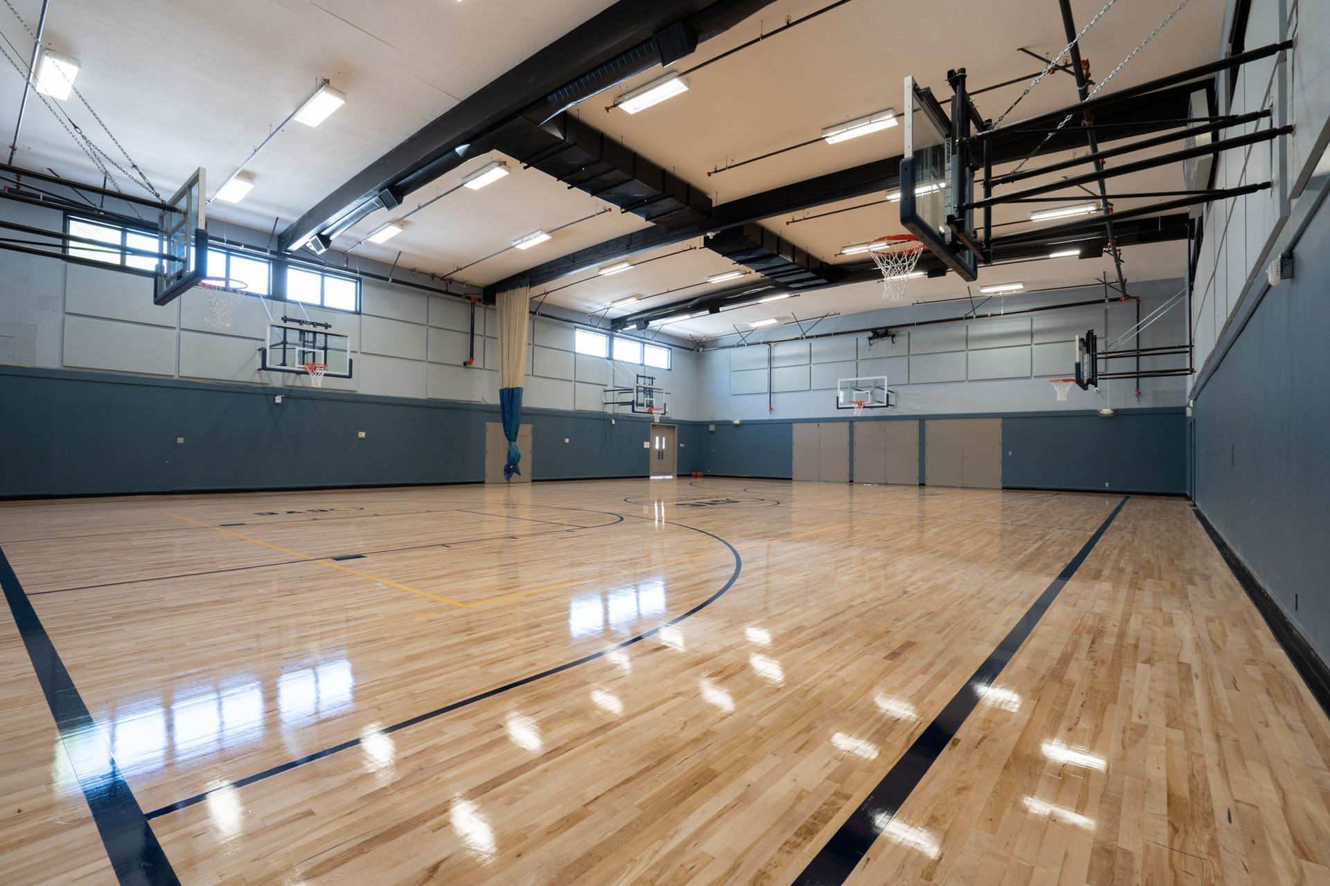 Empty indoor basketball court with polished wood floor, blue walls, and overhead lights