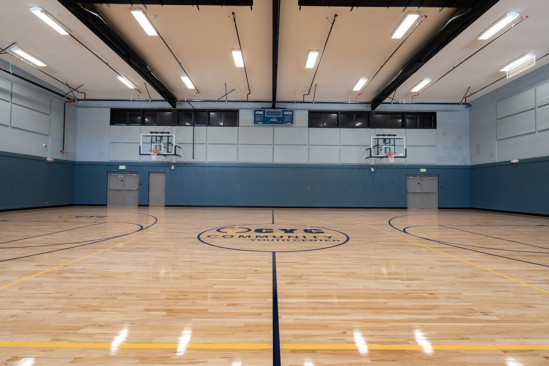 Empty indoor basketball court with polished wood floor, blue walls, and hoops on both ends