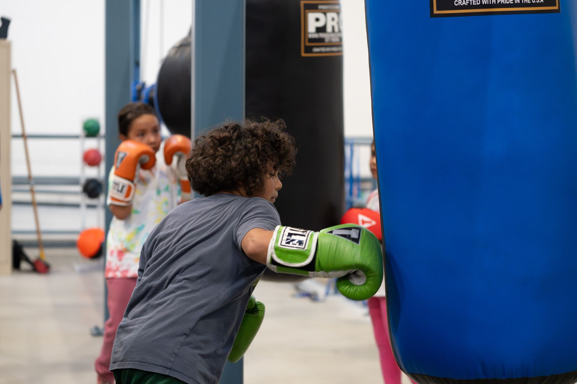 Child in green boxing gloves punching a blue training bag in a gym