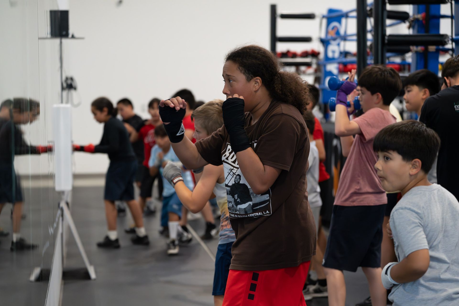 Children exercising in a gym, with one boy boxing in the foreground and others following along behind.