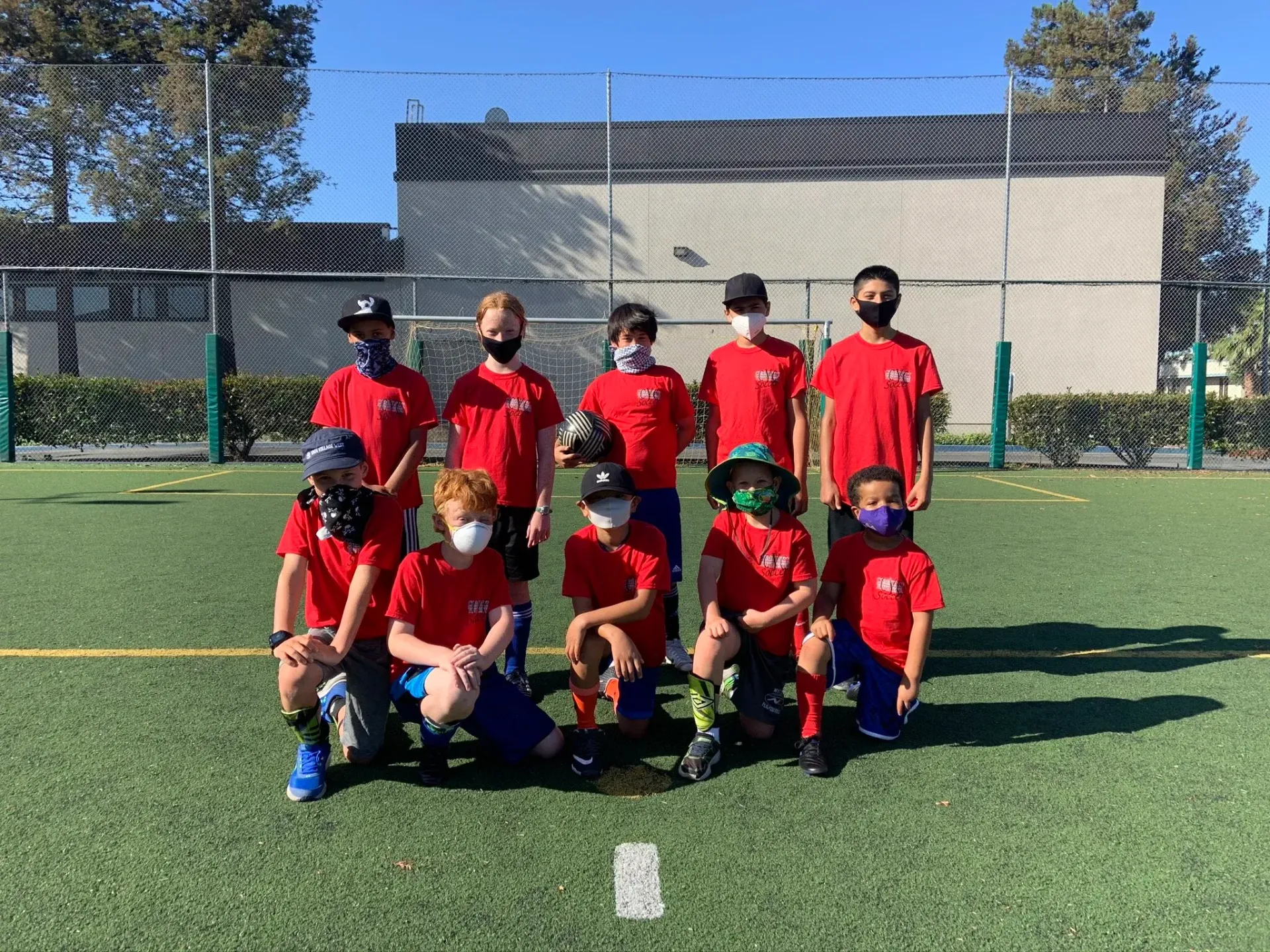 Youth soccer team in red jerseys posing on a field, with a goal and trees in the background.