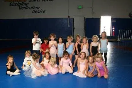 Group of children in ballet costumes posing on a blue gym floor in a dance studio