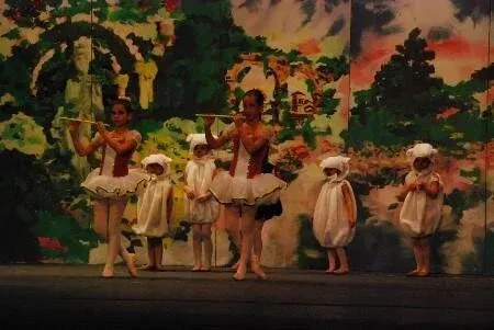 Children in white costumes performing a dance on a stage with a colorful jungle backdrop