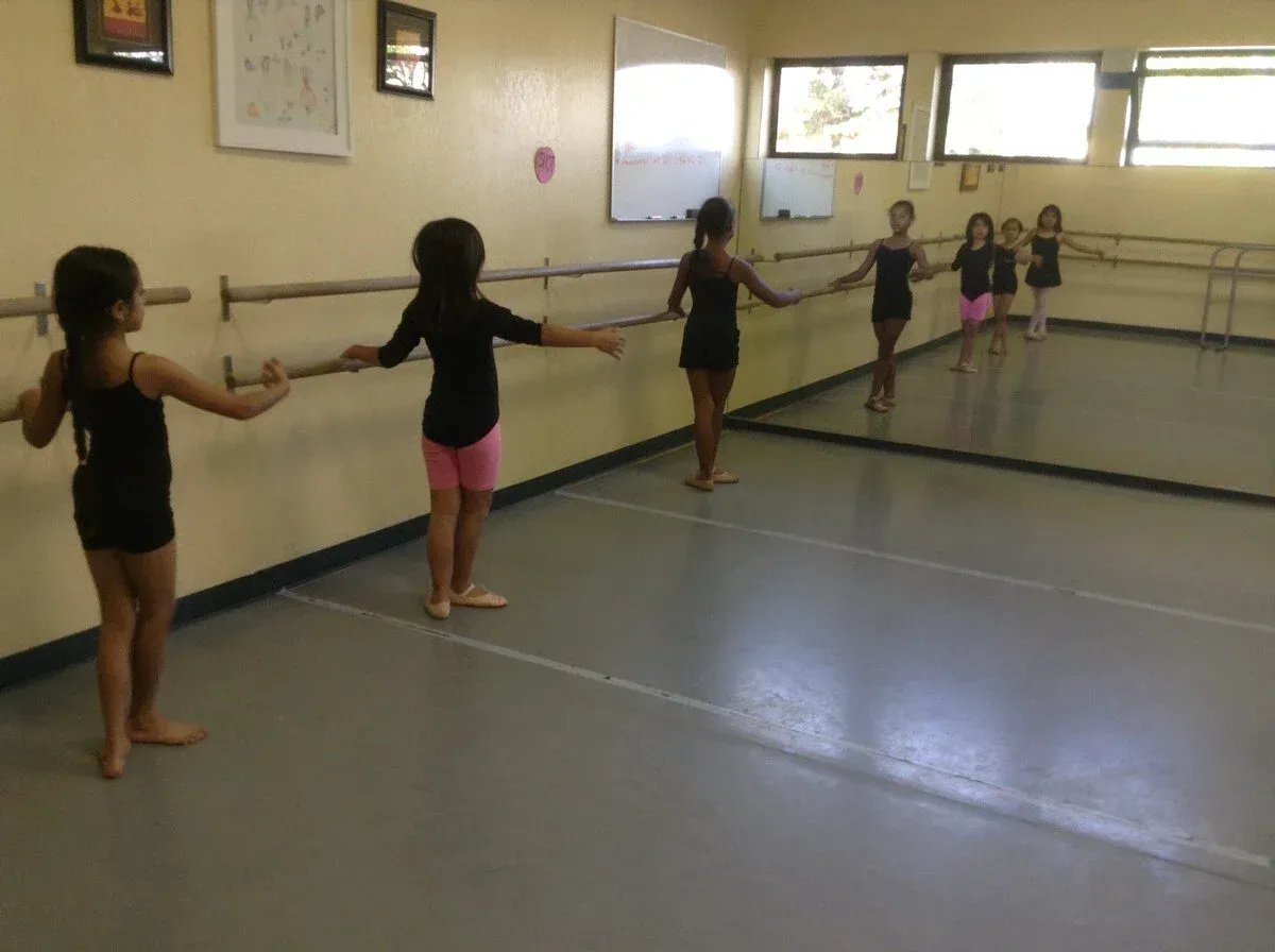 Young dancers holding a barre in a studio, practicing a ballet pose in a row