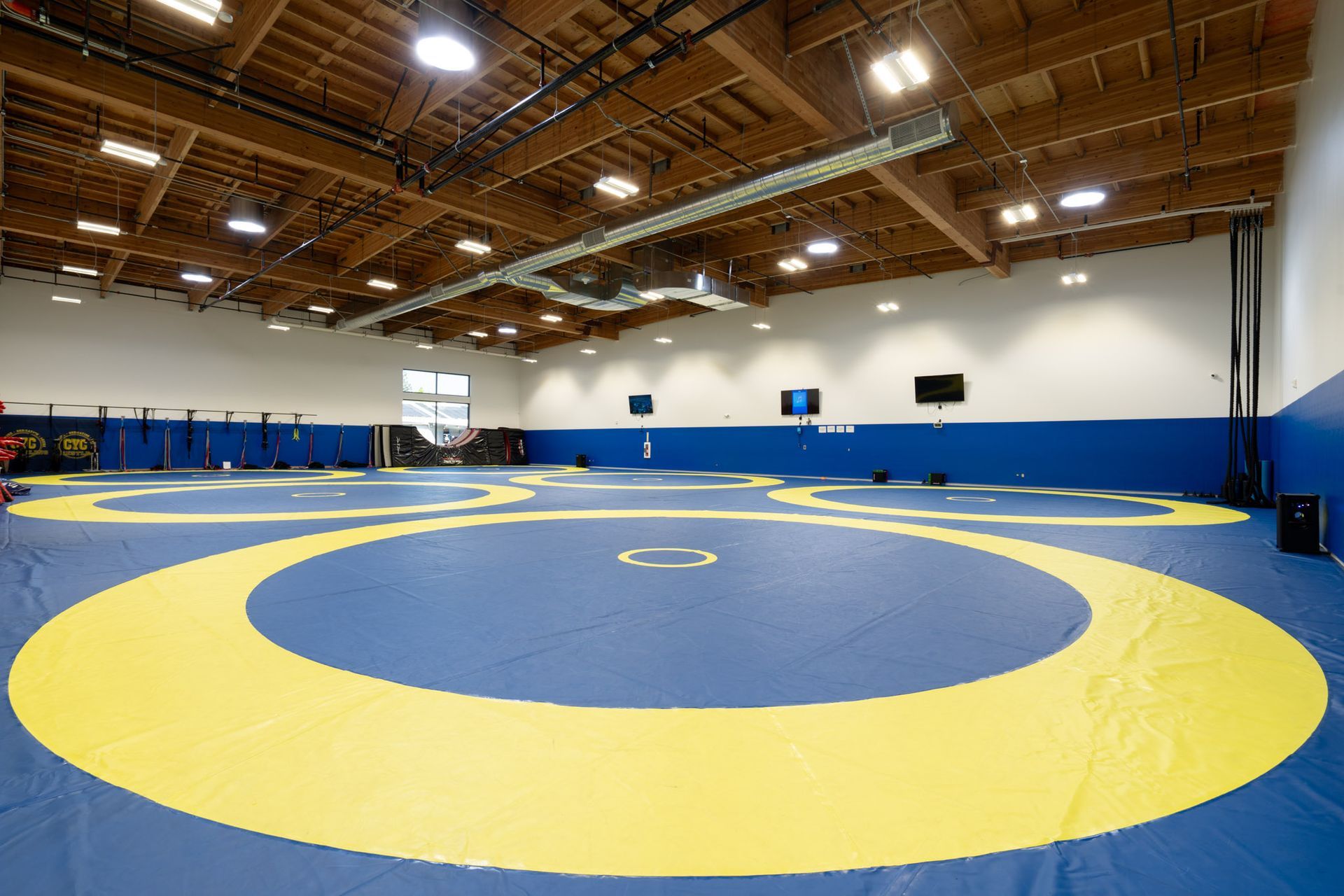 Empty indoor wrestling gym with yellow and blue mats under a wooden ceiling