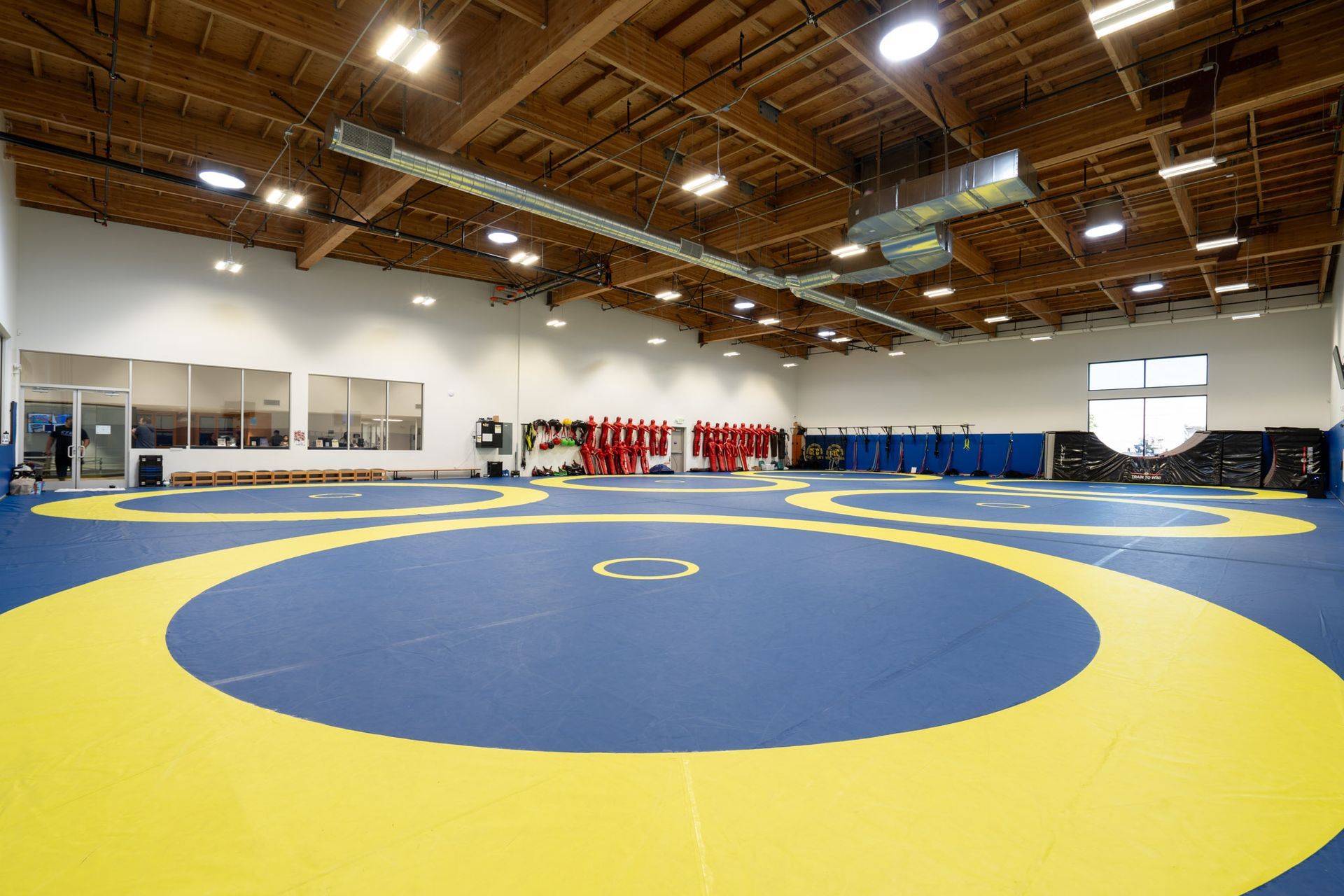 Empty indoor wrestling gym with a blue and yellow mat under wooden rafters.