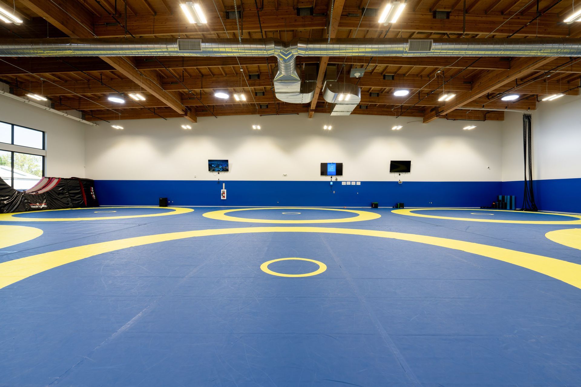 Empty wrestling gym with blue mats, yellow circles, and wooden ceiling lights