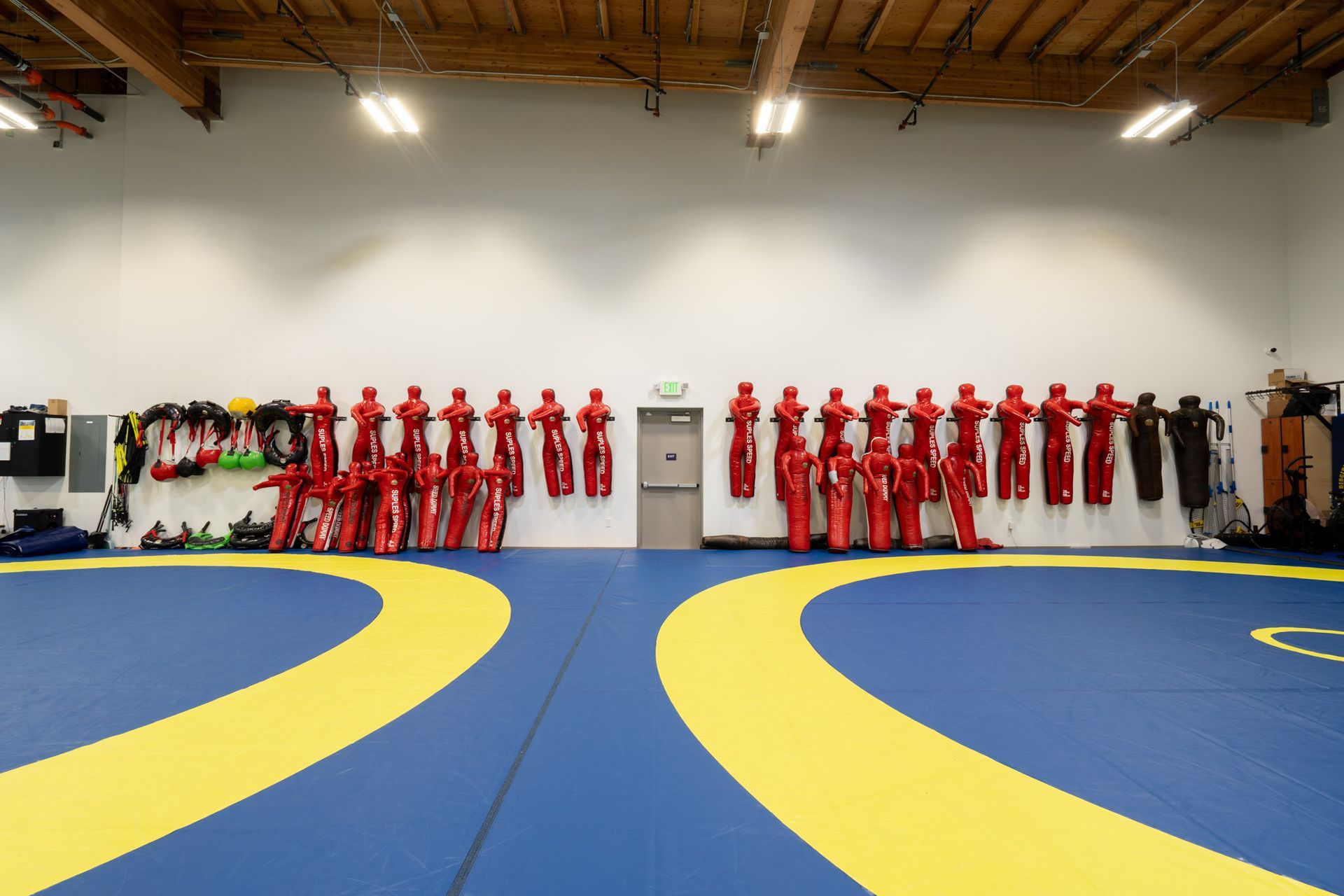 Wrestling gym with blue-and-yellow mats and rows of red singlets hanging on the wall