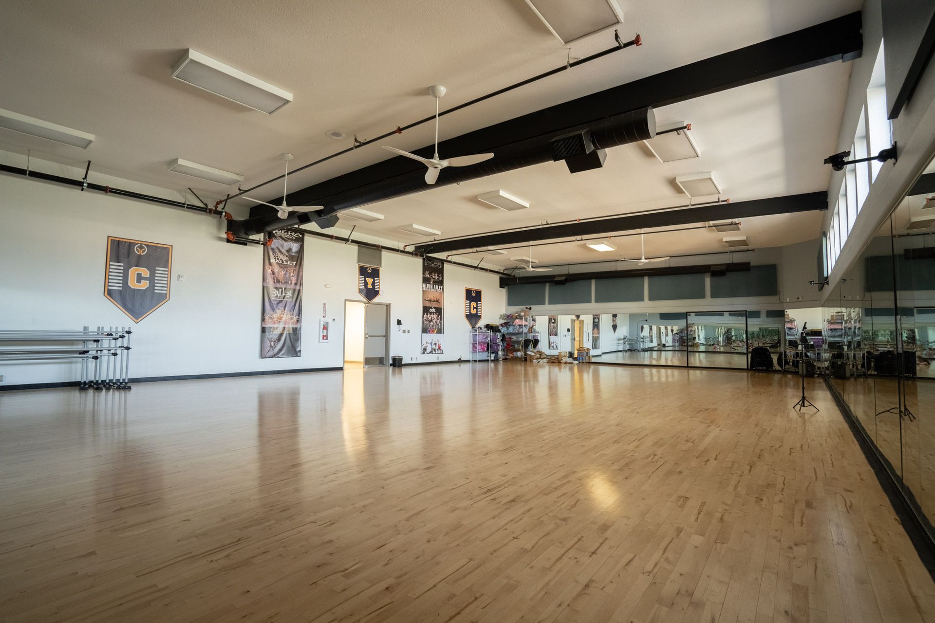 Empty dance studio with a polished wooden floor, mirrors, ballet barres, and high windows.