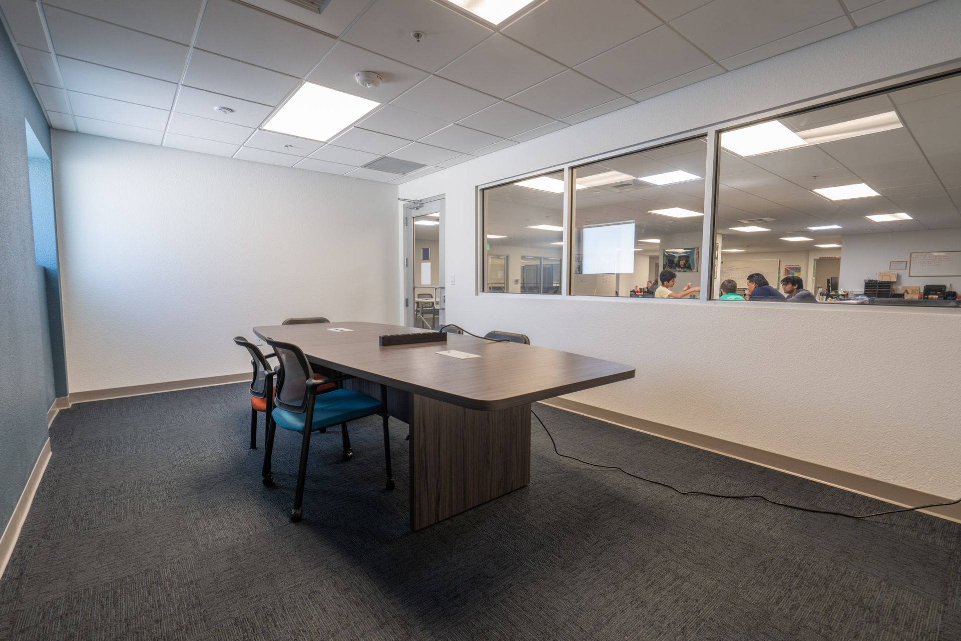 Modern office conference room with a table and chairs beside a glass-walled meeting area.