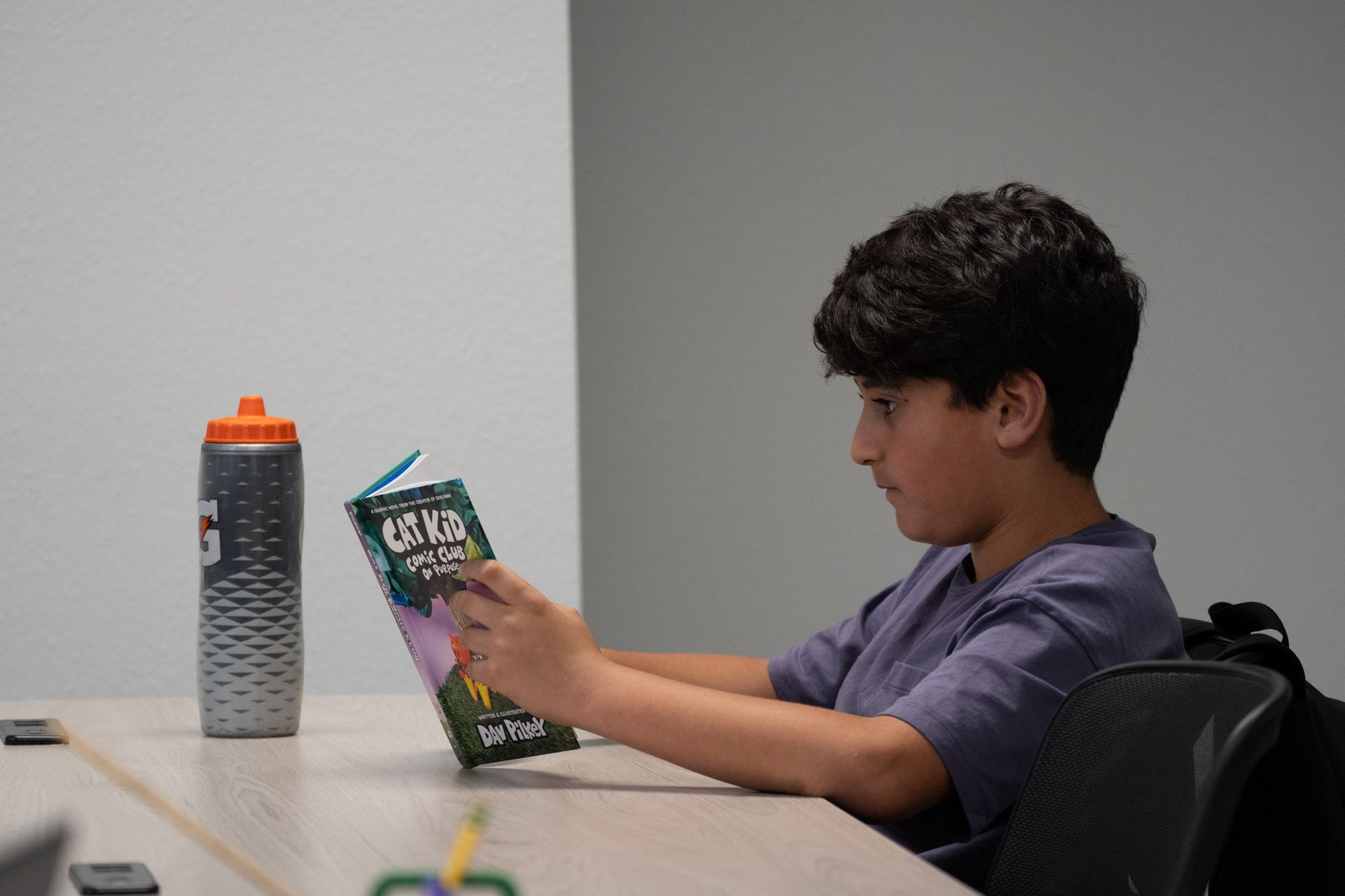 Boy reading a book at a table beside a large gray water bottle