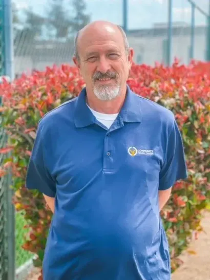 Man in blue polo shirt standing outdoors in front of red flowering bushes