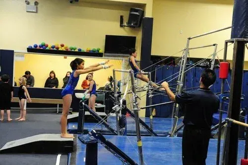 Gymnastics class with children practicing balance on parallel bars in a gym.