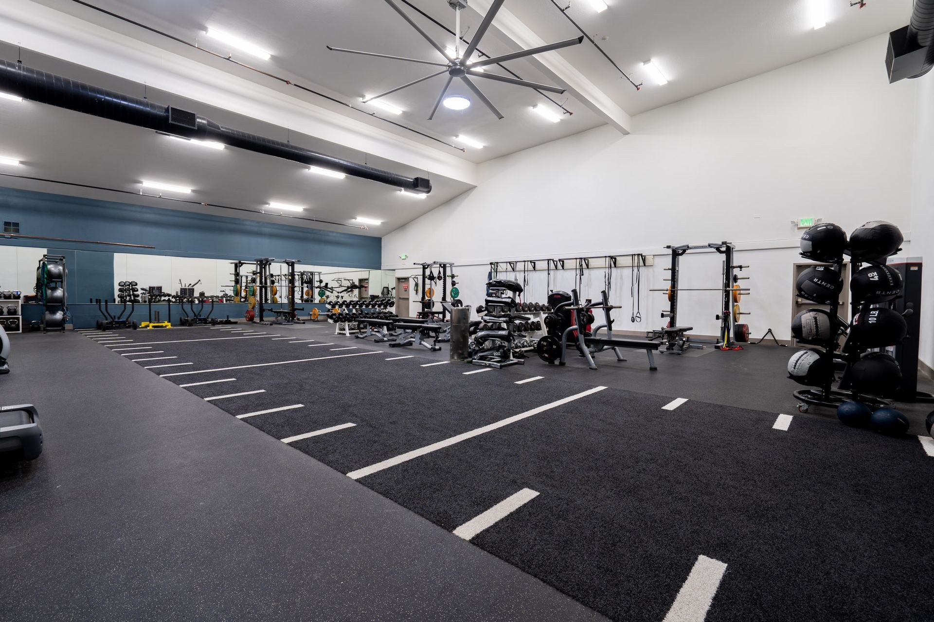 Empty gym with black turf, weight racks, and exercise equipment in a bright white room