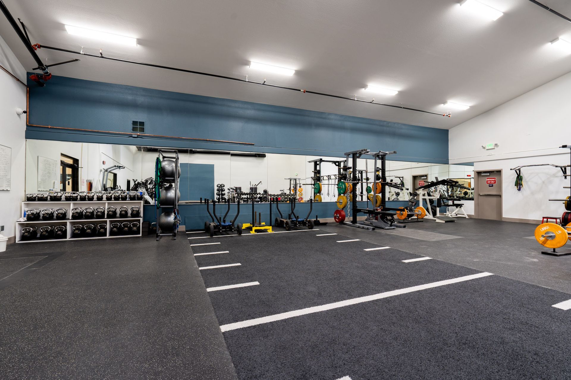 Empty indoor gym with black flooring, exercise equipment, and white walls with blue accents