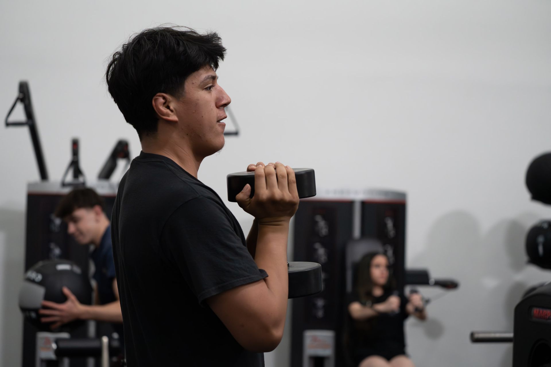 Person doing a seated dumbbell exercise in a gym, with others working out in the background