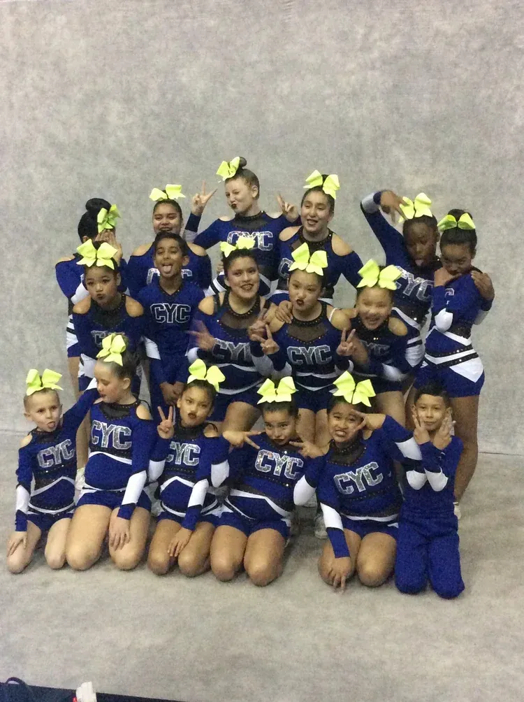 Youth cheer squad in blue uniforms posing with yellow bows against a gray backdrop