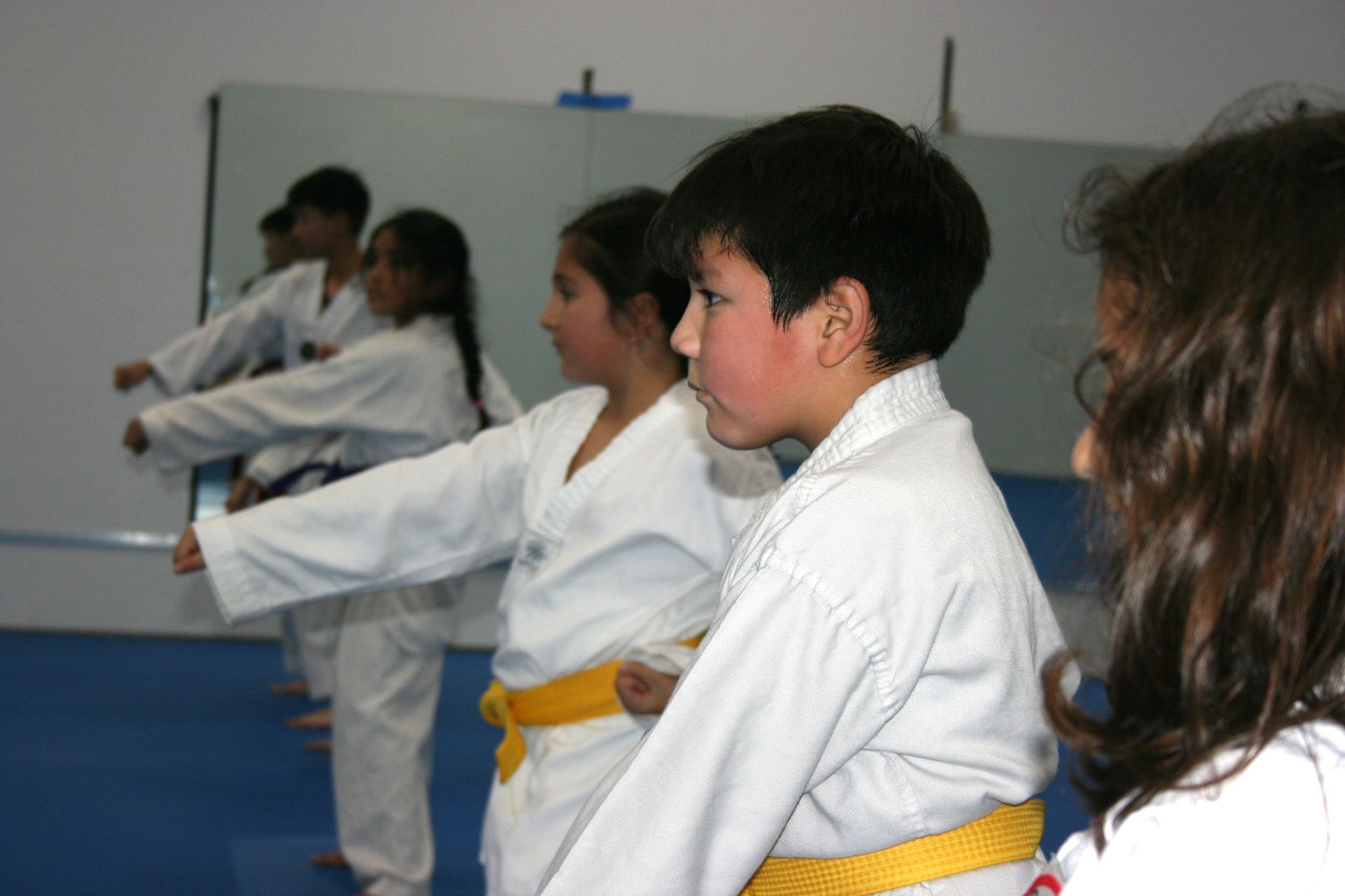 Children in white martial arts uniforms with yellow belts practicing in a row indoors