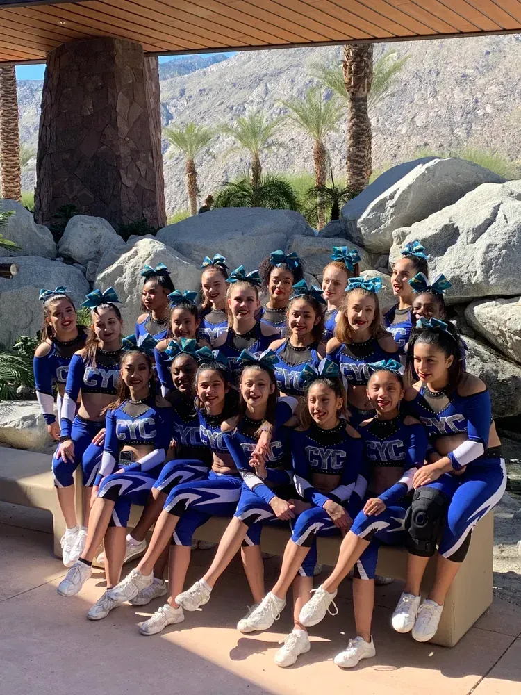 Group in blue uniforms seated outdoors under a shaded structure, smiling for a team photo