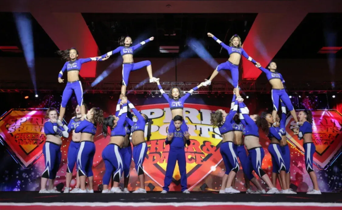 Cheer squad performing a synchronized stunt on a brightly lit stage with red and blue backdrop