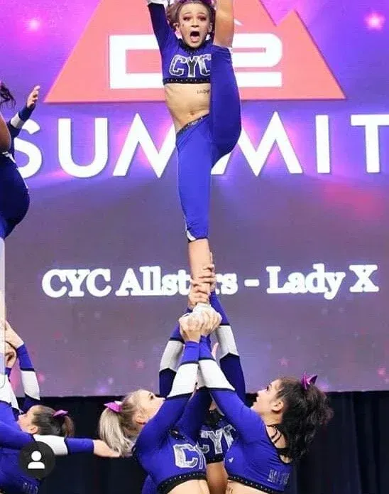 Cheerleaders performing a stunt on stage at the C2 Summit, with one flyer held high above the group