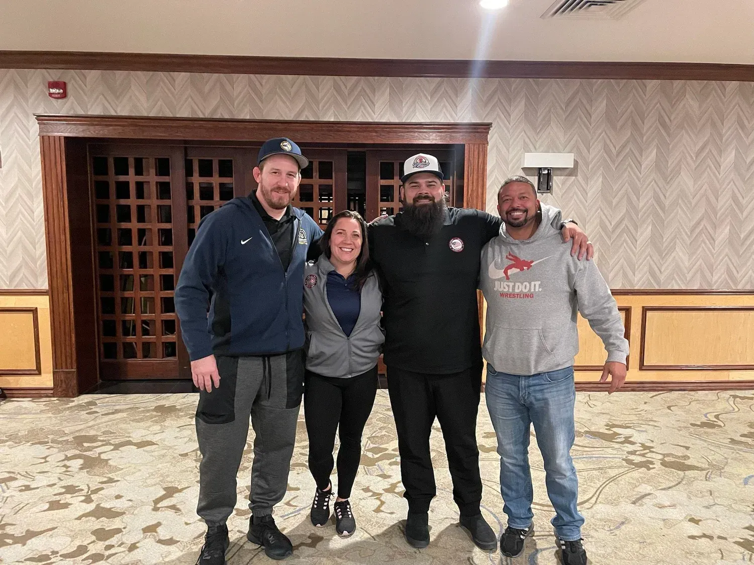 Four people posing together in a hotel lobby, standing on patterned carpet in casual clothes.
