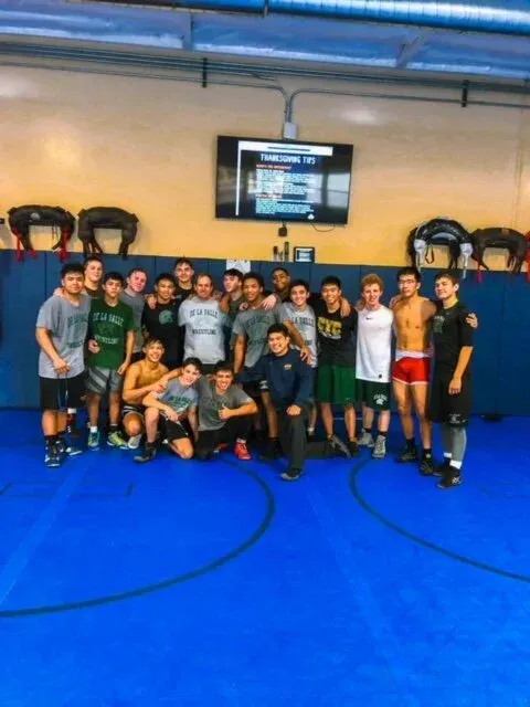 Group of athletes posing together in an indoor gym with bright blue mats and exercise equipment behind them