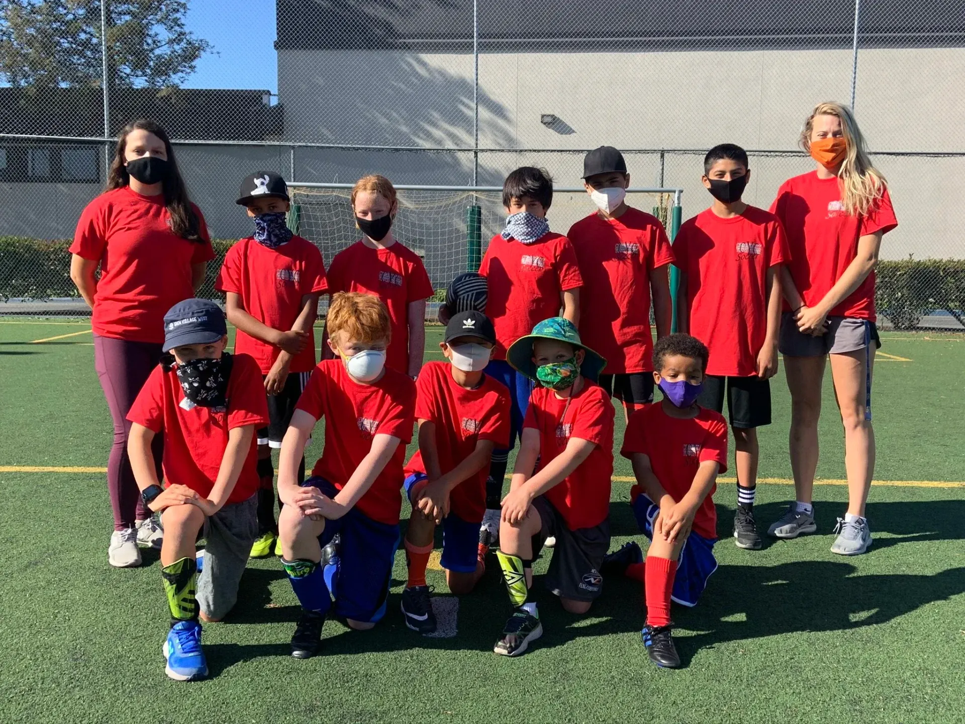 Youth soccer team in red uniforms posing on a field with coaches behind them