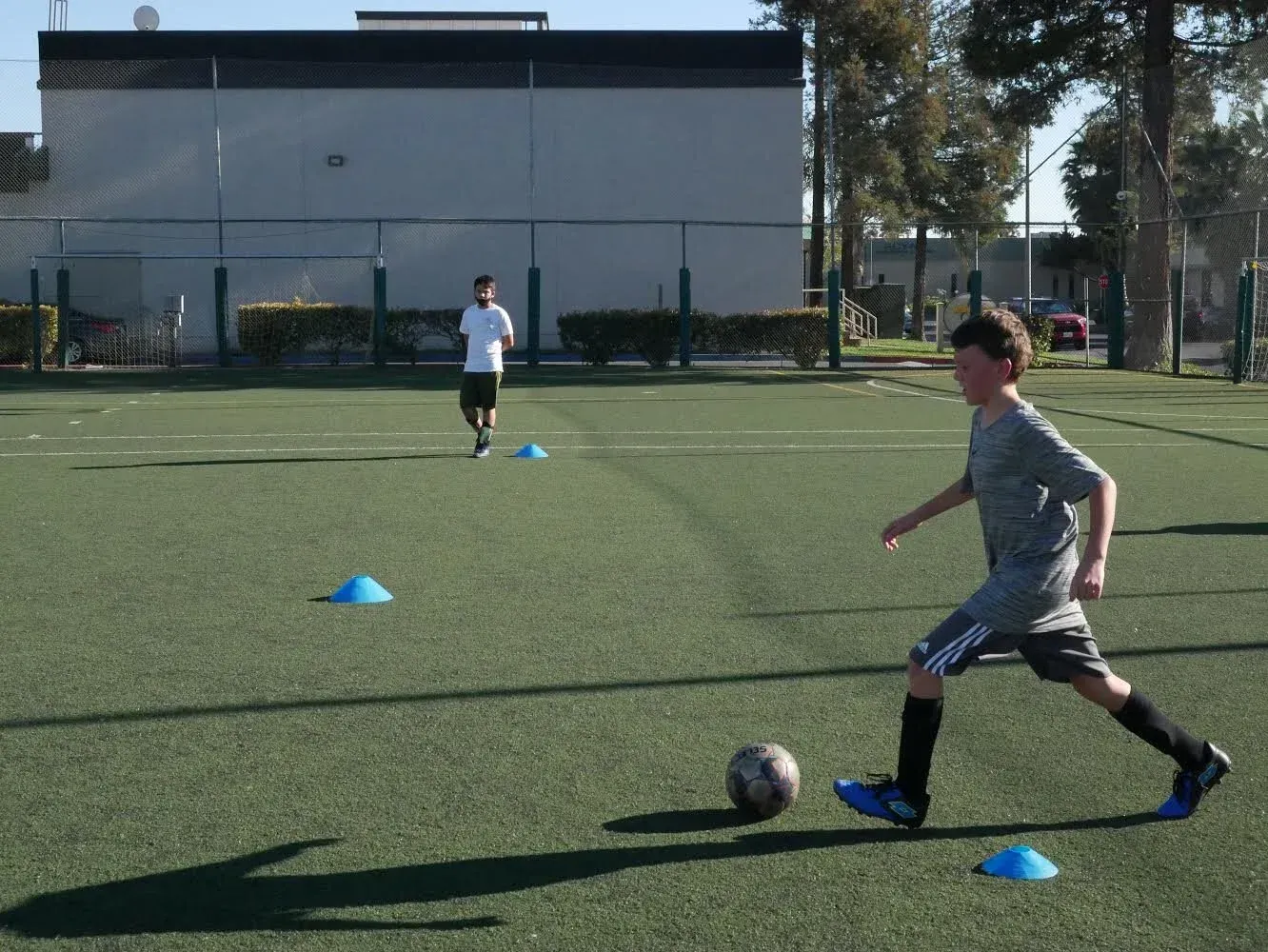 Soccer players practicing dribbling on a field with blue cones in bright sunlight