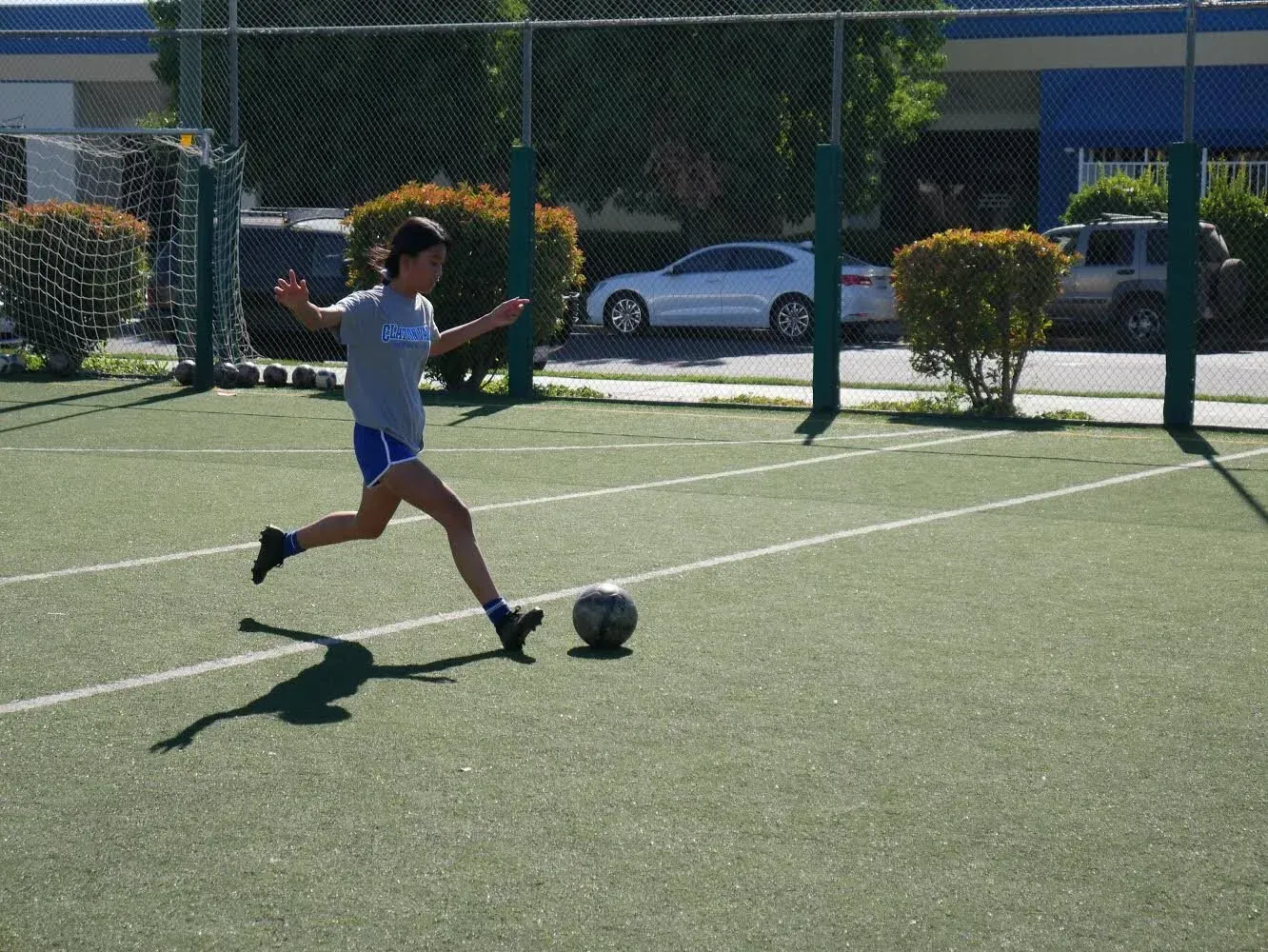 Soccer player in a white shirt kicks a ball on a sunny outdoor field.