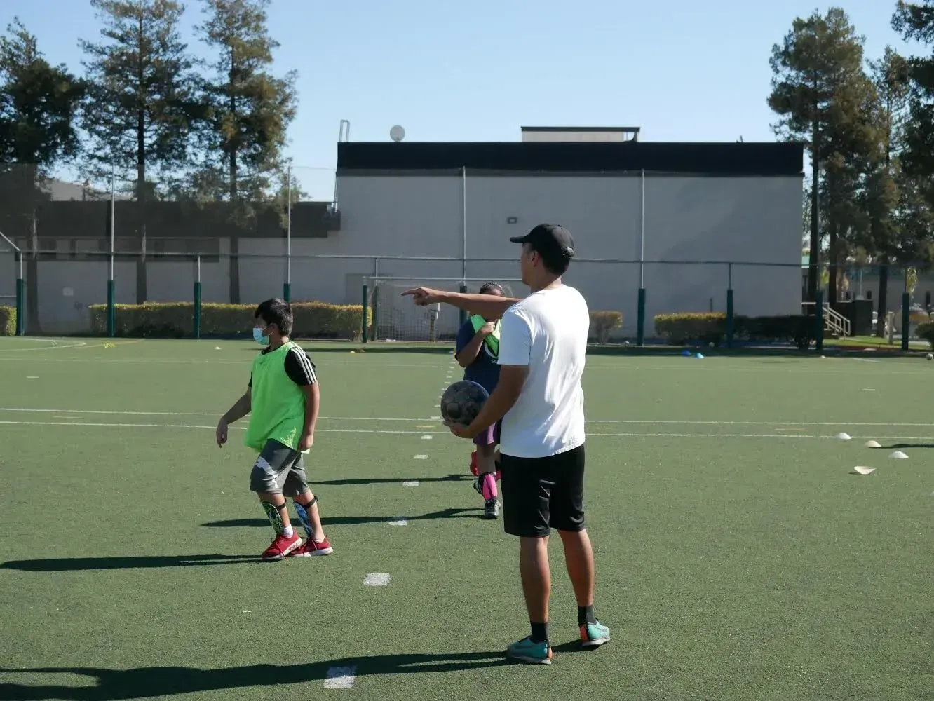 People on a soccer field, one pointing while others stand nearby under bright sunlight.