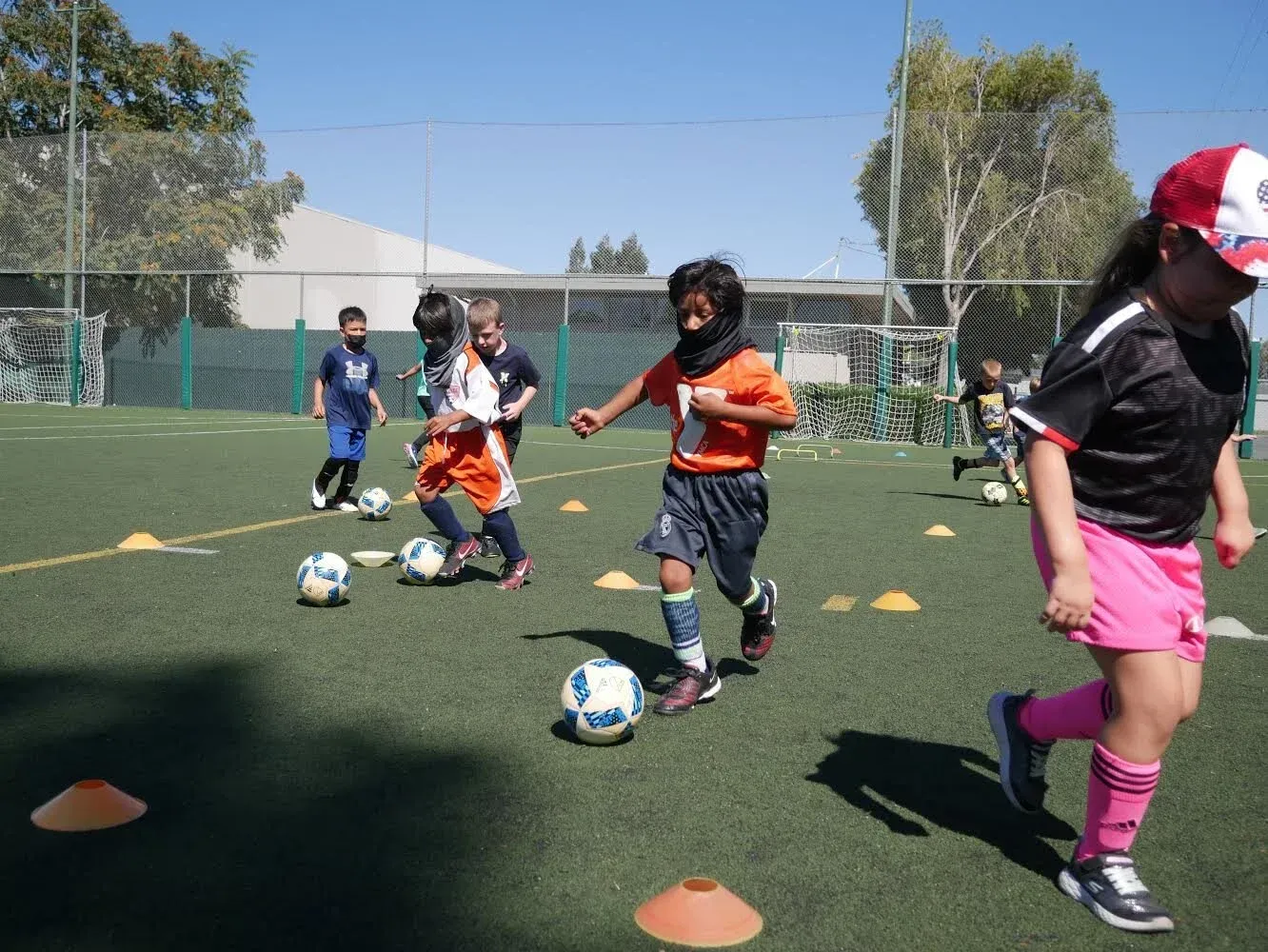 Children practicing soccer drills with cones on a grassy field under sunny skies