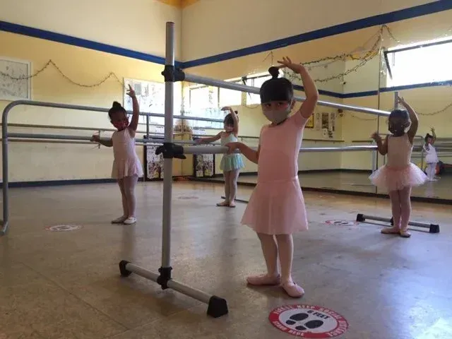 Young ballet students in pink leotards practicing at the barre in a dance studio