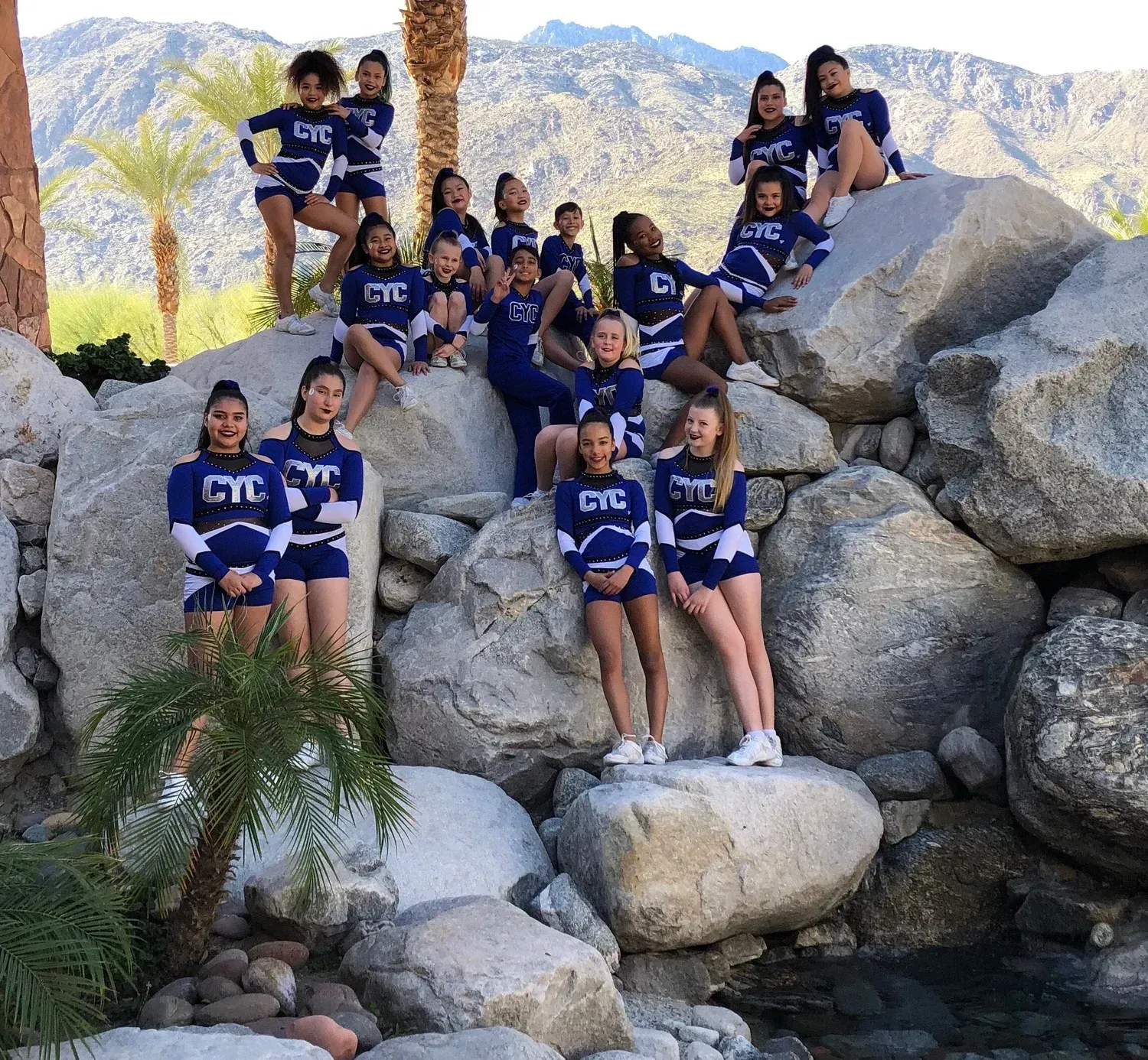Youth team in navy uniforms posing on large rocks with mountains in the background