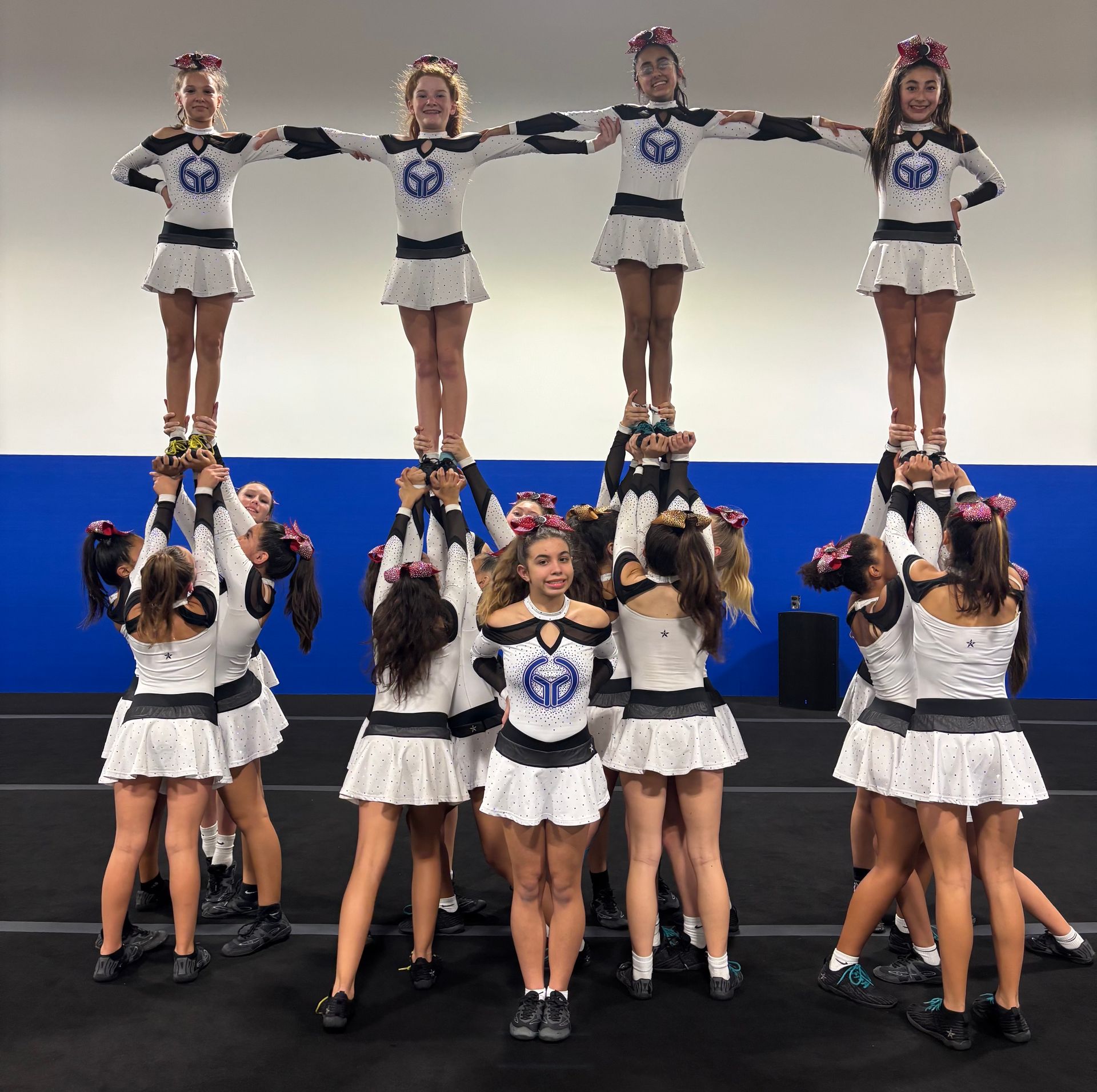 Cheer team performing a stunt routine on stage, lifting four members overhead in matching blue and white uniforms