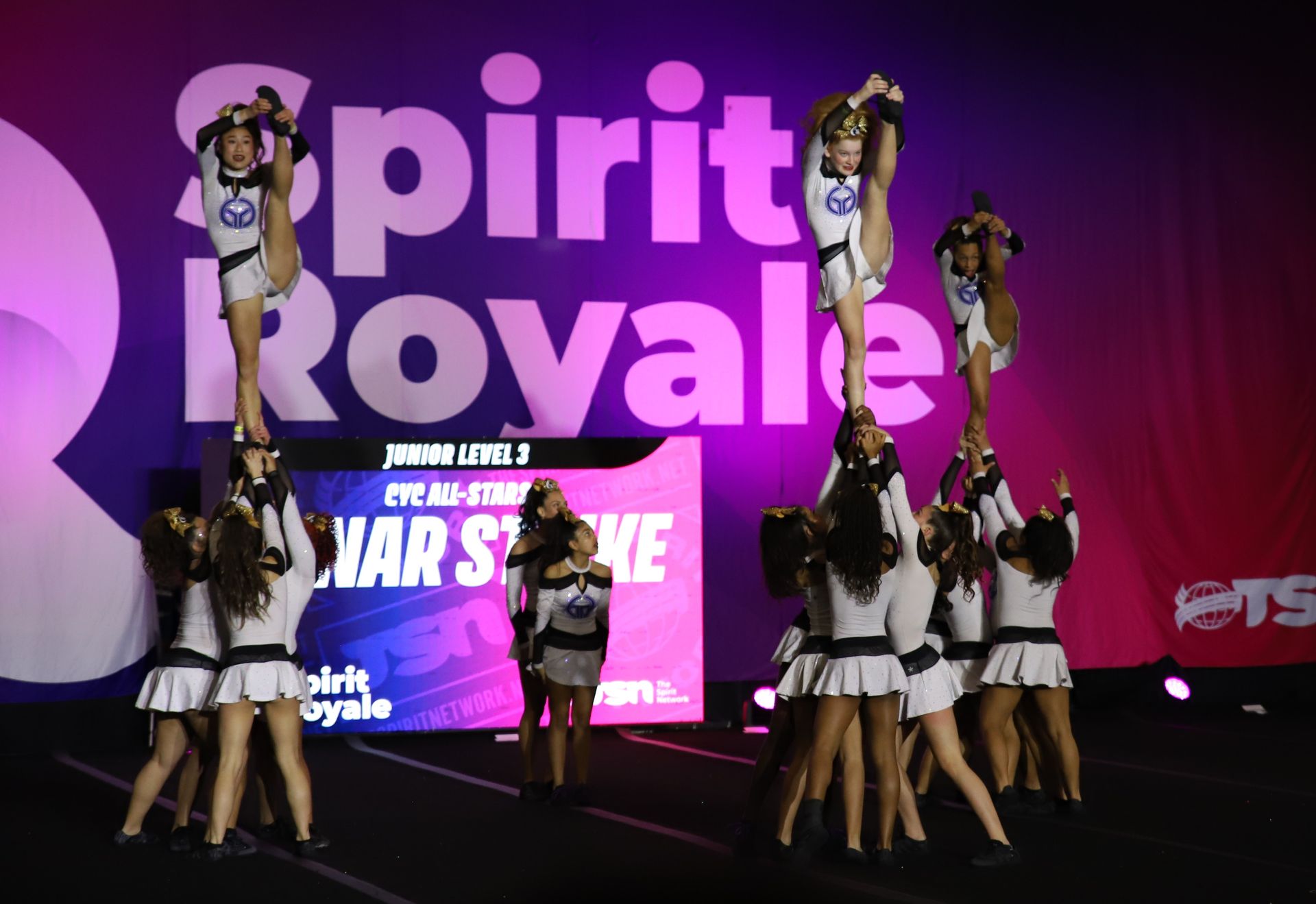 Cheerleaders posing in formation on stage at Spirit Royale, with purple and pink event lighting.
