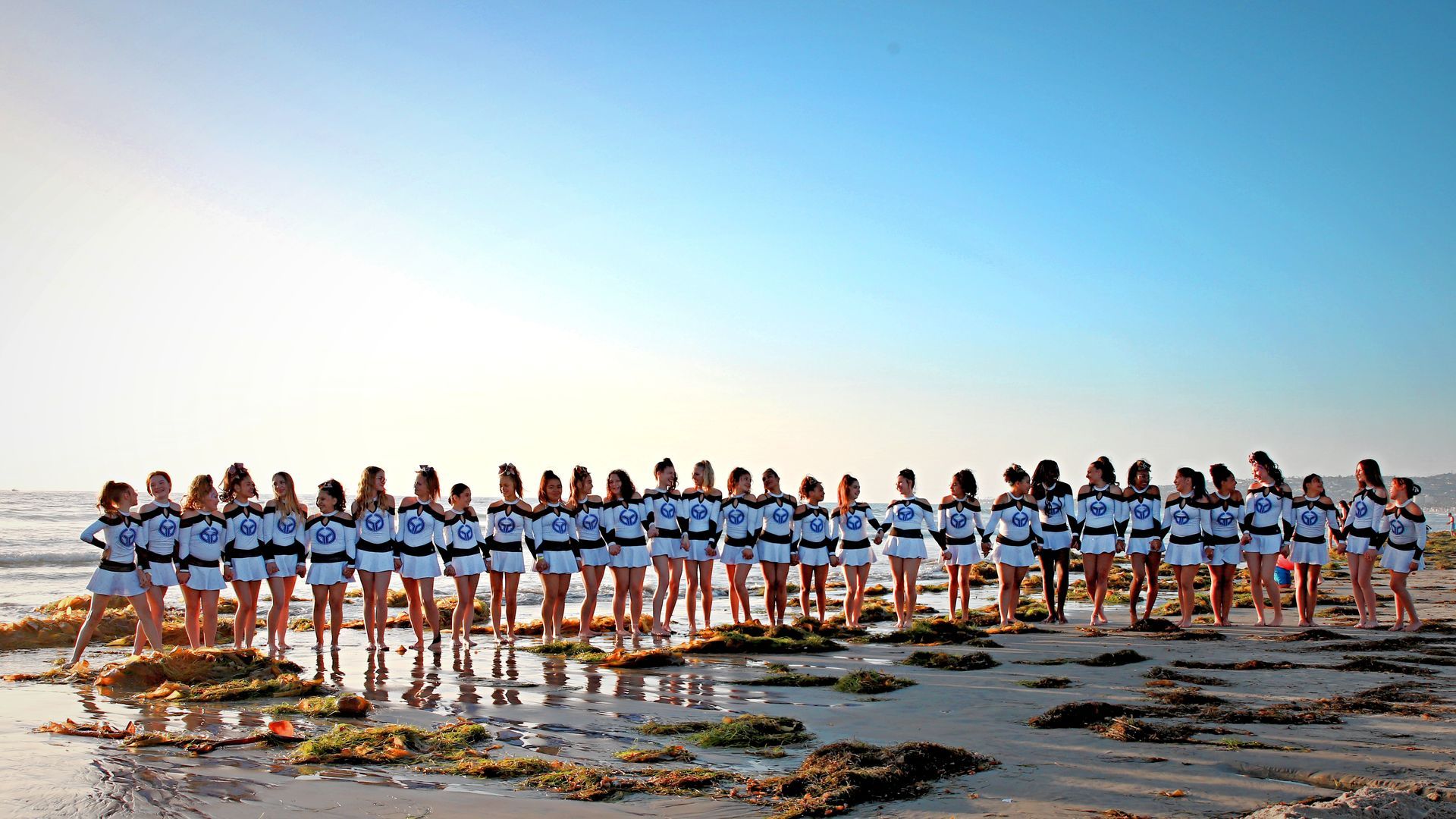 Group of people in matching blue shirts standing in a line on a beach at sunset.
